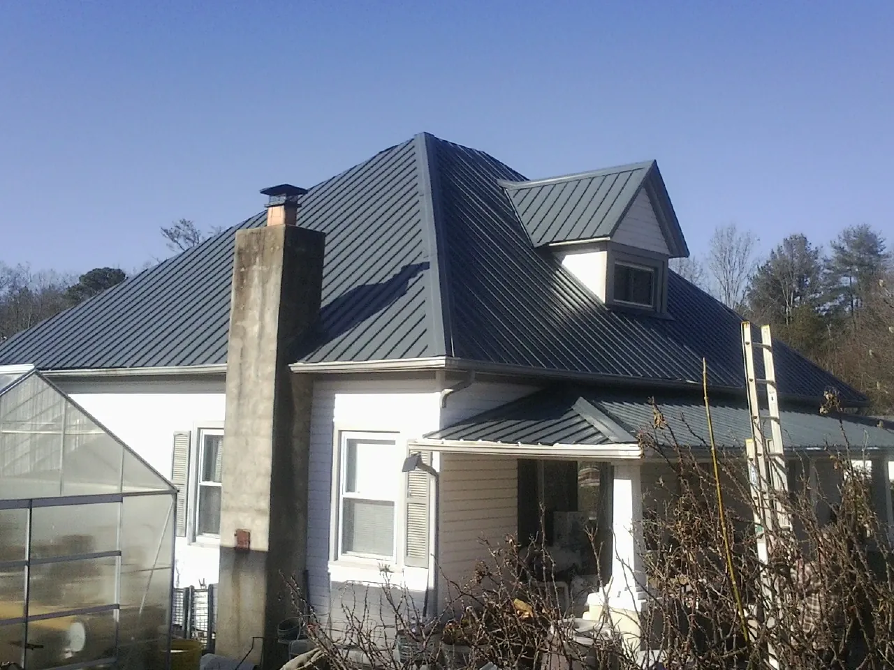 Dark blue standing seam metal roof on a white farmhouse with dormer — Slate & Tile Roof Repair by Roofing Brothers in Sykesville