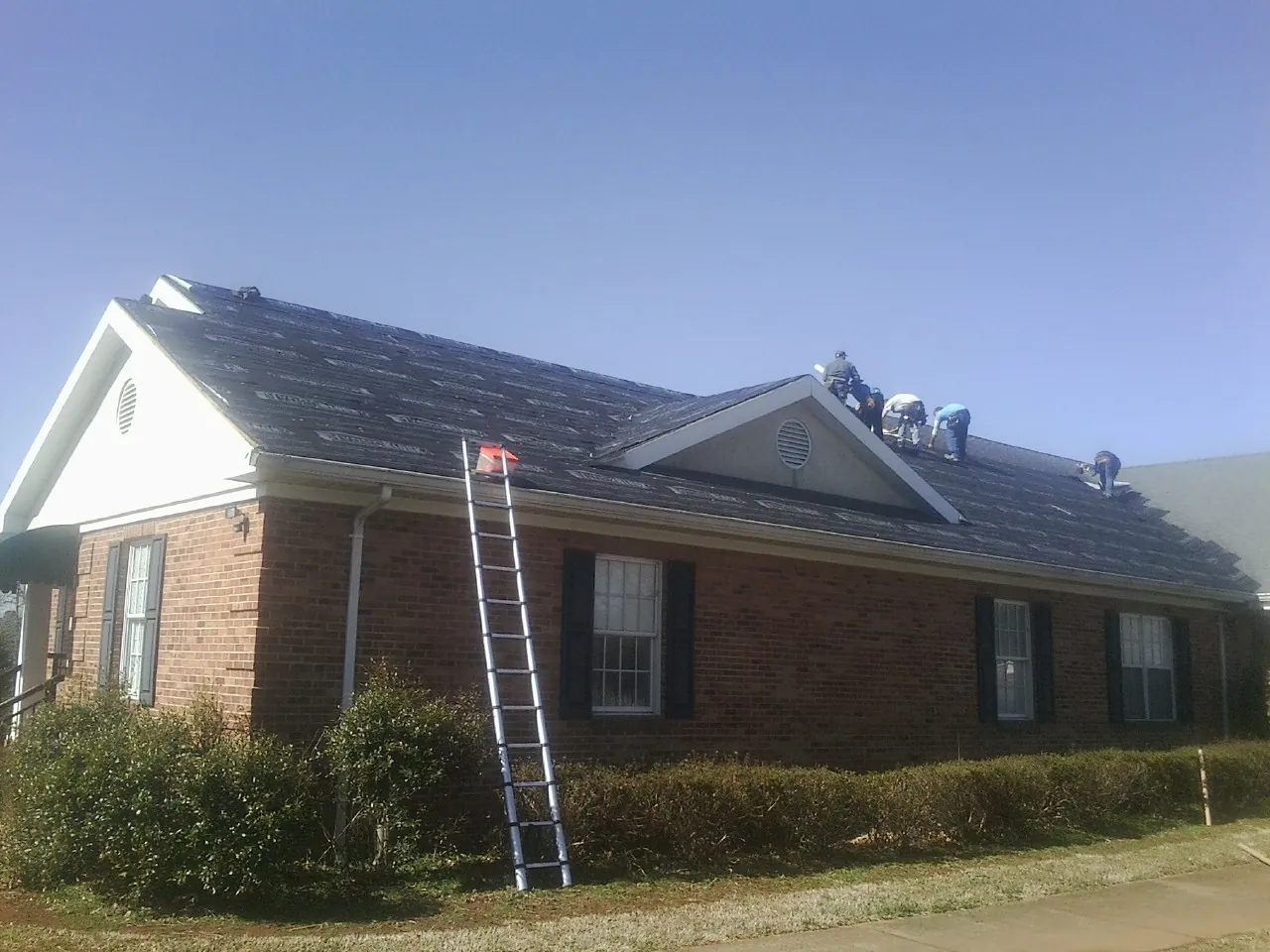 Crew tearing shingles off a brick ranch roof with a ladder set — Metal Roof Repair work by our crew in Sykesville
