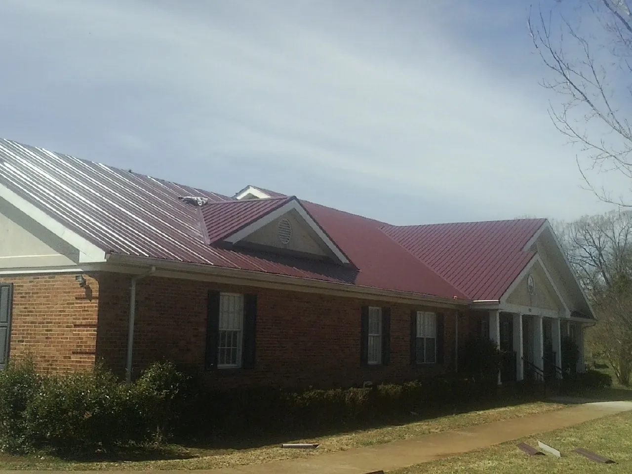 Red metal roof with gabled entries on a long brick building, from a Hail Damage Roof Repair job in Sykesville