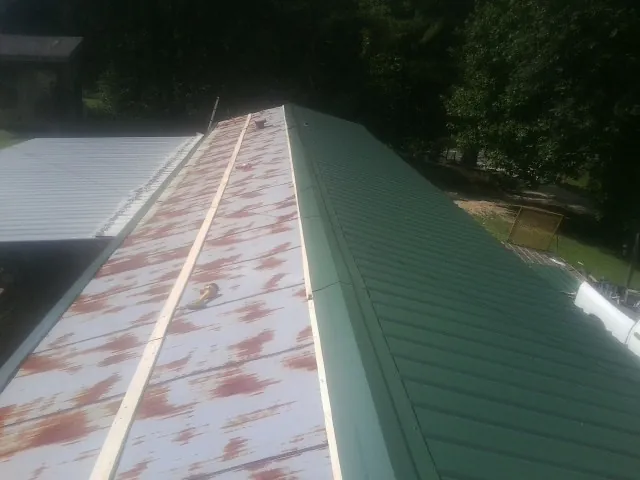 Old rusted panels beside newly installed green metal roofing — Wind Damage Roof Repair by Roofing Brothers in Sykesville