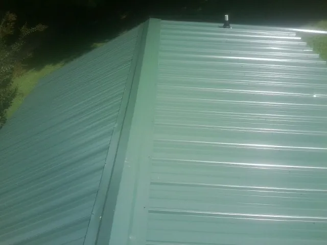 New green metal panels meeting at the ridge of a roof — Flat Roof Repair work by our crew in Sykesville
