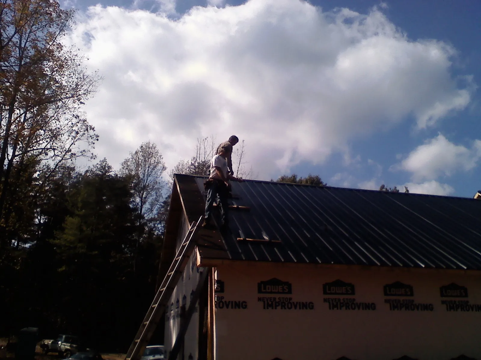 Roofer fastening dark metal panels high against a cloudy sky, from a Roof Inspection job in Sykesville