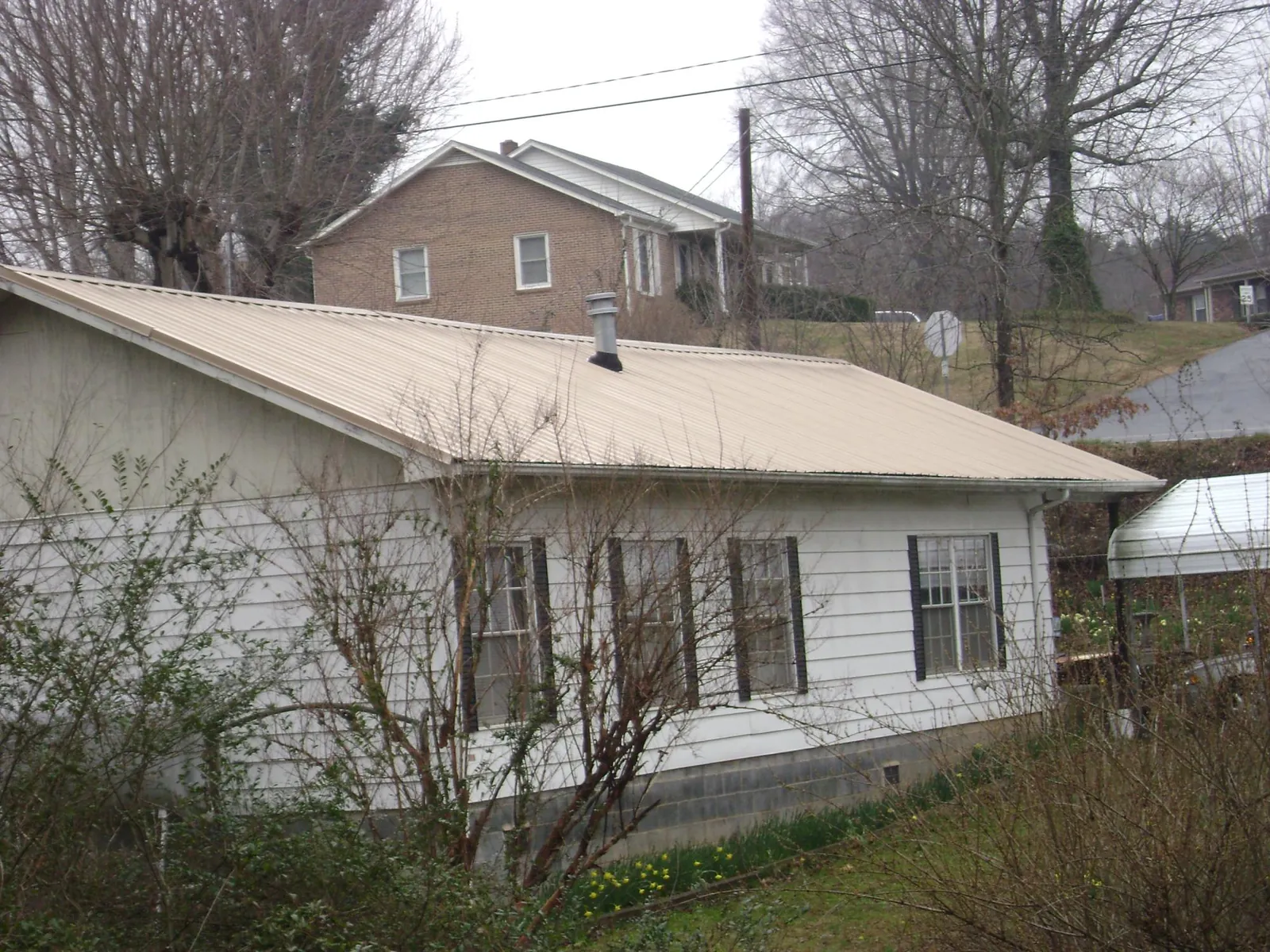 Tan metal roof on a white sided house set into a hillside — Commercial Roofing by Roofing Brothers in Sykesville